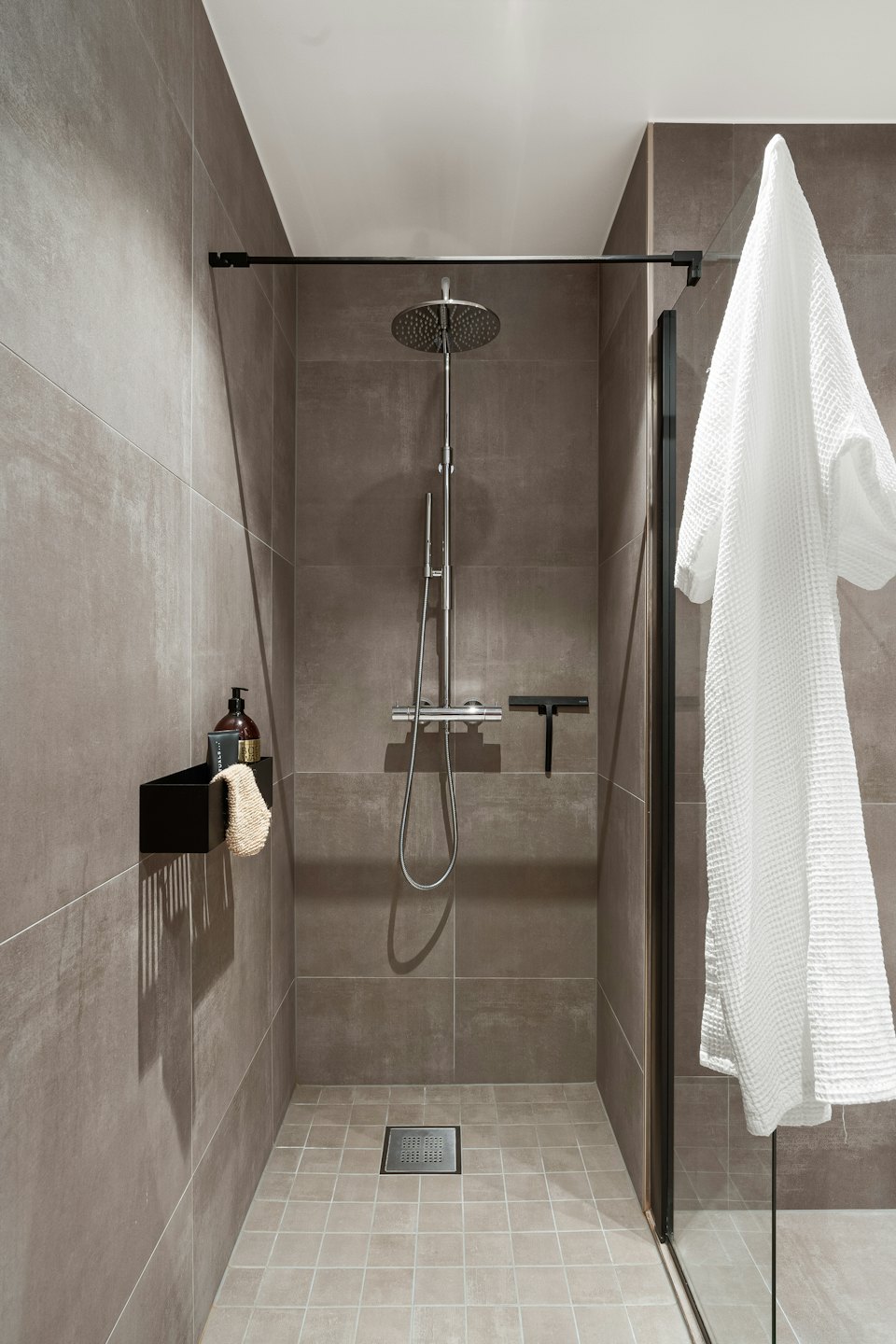 Moderne begehbare Dusche mit Badeprodukten und einem hängenden Bademantel.
